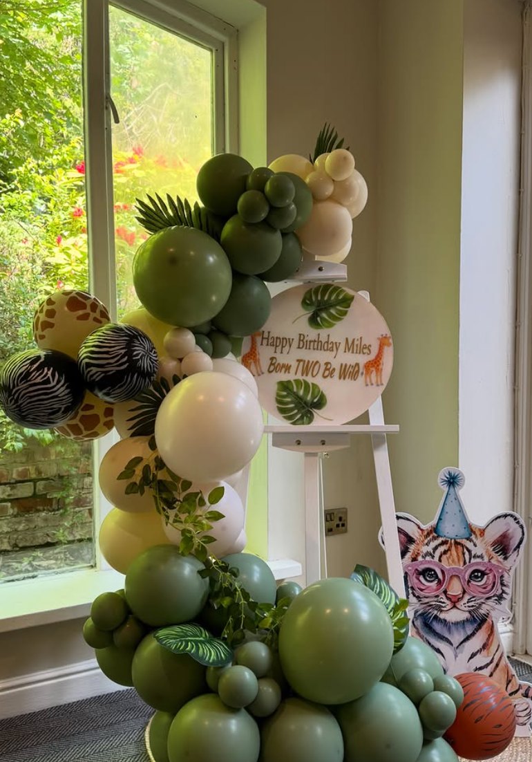 Jungle themed green balloon garland with animal print balloons and an easel sign