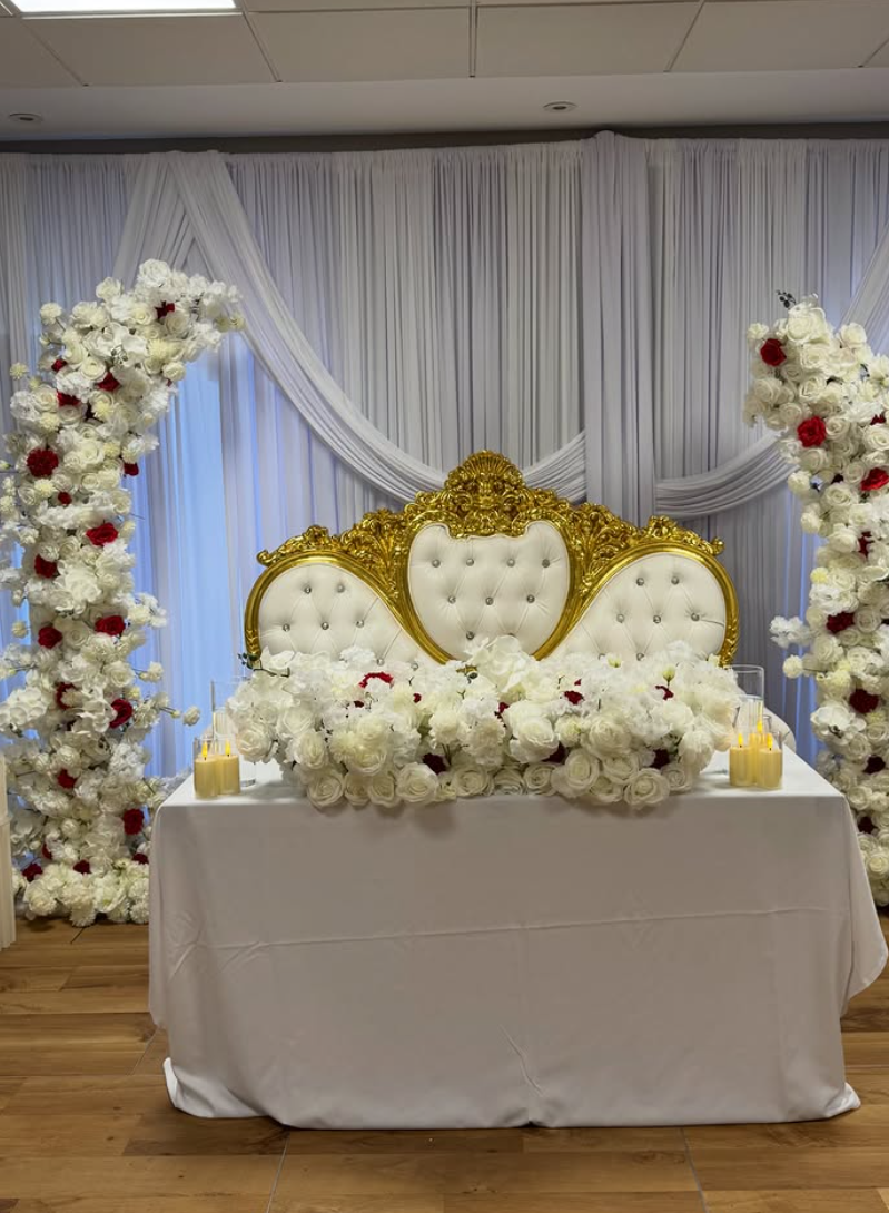 White and red floral arches framing a gold and white throne set behind a floral top table
