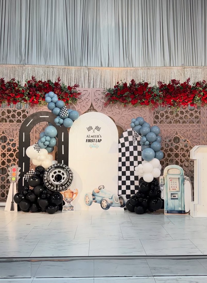 Race car themed backdrop set with checkered flags, road arch and blue balloon garlands